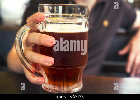 Dunkles Bier in mans hand, Becher Bier, Stockfoto