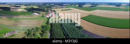 Luftaufnahme der Felder, Wiesen und Wälder mit einer Straße in der Mitte und einem kleinen Dorf im Hintergrund, drone Landschaft Stockfoto