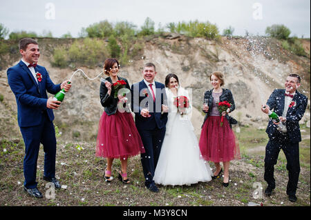 Hochzeit paar, Trauzeuge und Brautjungfern am besten Mann Öffnen der Flasche Champagner im Sand Steinbruch suchen. Stockfoto