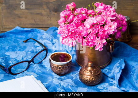 Rosa Rosen und eine Tasse Kaffee in einem Kupfer Schale Stockfoto