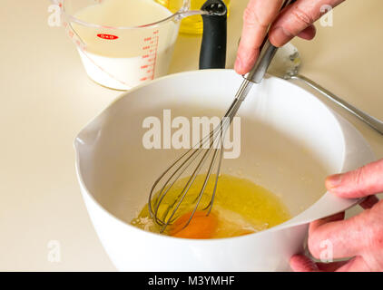 Mann schlagen Mischung mit Schneebesen Pfannkuchenteig für Faschingsdienstag mit Mehl, Milch, Eier und Öl in einer Küche zu Hause Stockfoto