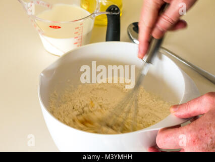 Mann schlagen Mischung mit Schneebesen Pfannkuchenteig für Faschingsdienstag mit Mehl, Milch, Eier und Öl in einer Küche zu Hause Stockfoto