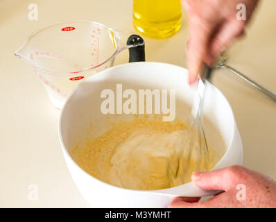 Mann schlagen Mischung mit Schneebesen Pfannkuchenteig forShrove Dienstag mit Mehl, Milch, Eier und Öl in einer Küche zu Hause Stockfoto