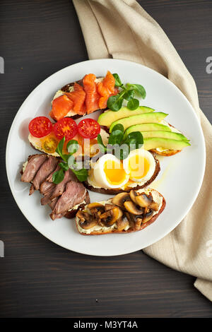 Bruschetta, sortiert, verschiedene Füllungen, auf Platten mit einem weich gekochten Ei in der Mitte Stockfoto