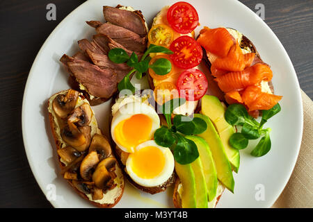 Bruschetta, sortiert, verschiedene Füllungen, auf Platten mit einem weich gekochten Ei in der Mitte Stockfoto