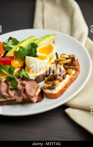 Bruschetta, sortiert, verschiedene Füllungen, auf Platten mit einem weich gekochten Ei in der Mitte Stockfoto