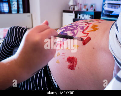 Kleine Tochter Malerei Mütter schwangere Bauch mit Pinsel zu Hause Nahaufnahme Stockfoto