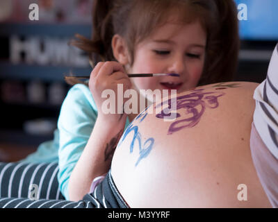 Kleines Mädchen Malerei Mütter Bauch und lächelnd zu Hause Stockfoto