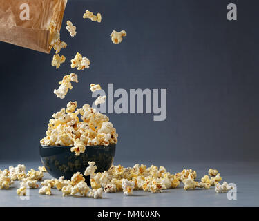 Popcorn fliegen in die Schüssel aus braunem Papier Paket über grauen Hintergrund. Platz für Ihren Text