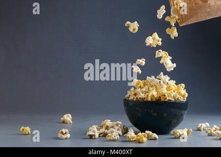 Popcorn fliegen in die Schüssel aus braunem Papier Paket über grauen Hintergrund. Platz für Ihren Text Stockfoto