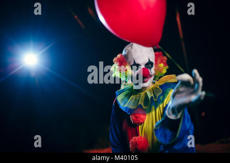 Foto von Clown mit roten Luftballon auf dem Hintergrund der brennenden Laterne Stockfoto