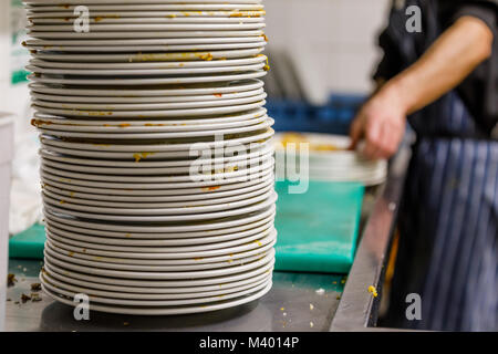 Stapel von schmutzige Teller in einem Restaurant Küche mit männlichen Arbeitnehmers Abwasch im Hintergrund Stockfoto