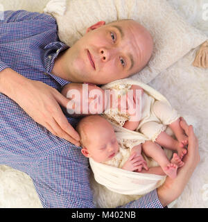 Vater liegen auf einem Flokati hält seine eineiigen Zwillingen von 3 Wochen alt Stockfoto