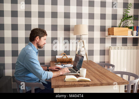 Junger Mann in seinem Wohnzimmer auf einem Laptop arbeiten Stockfoto