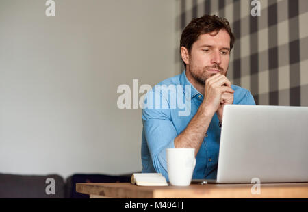 Junger Mann, der an einem Notebook arbeitet in seinem Wohnzimmer Stockfoto