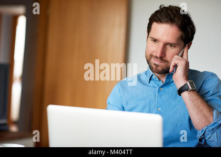 Lächelnd Mann auf ein Handy, während die von zu Hause aus arbeiten Stockfoto