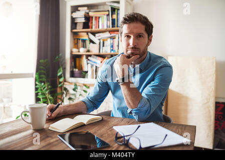 Junge Mann in seinem Wohnzimmer Tisch zu Hause arbeiten Stockfoto