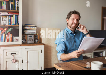 Mann Lesen von Dokumenten und Gespräche am Mobiltelefon zu Hause Stockfoto