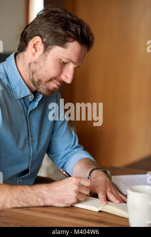 Junger Mann schreiben in einem Notebook während der Arbeit von zu Hause aus Stockfoto