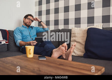 Junger Mann auf seinem Sofa mit einem digitalen Tablet Stockfoto