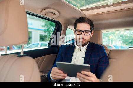 Erfolgreiche junge Unternehmer mit einem digitalen Tablet in seinem Auto Stockfoto