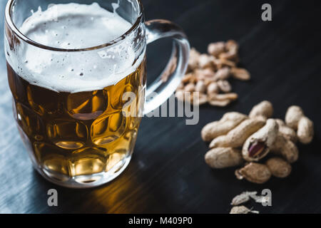 Glas Bier und Erdnüsse auf dem dunklen Hintergrund Stockfoto