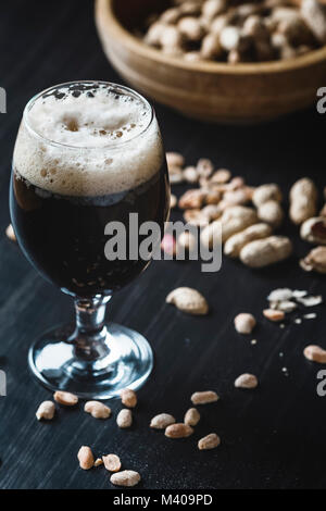 Glas Bier und Erdnüsse auf dem dunklen Hintergrund Stockfoto