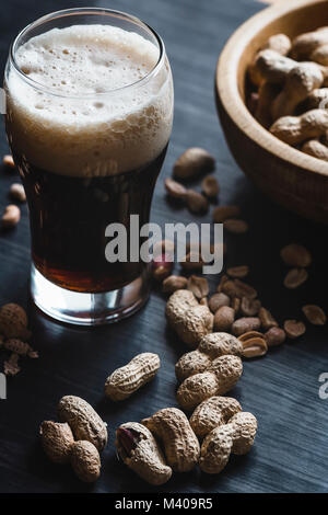 Glas Bier und Erdnüsse auf dem dunklen Hintergrund Stockfoto