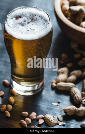 Glas Bier und Erdnüsse auf dem dunklen Hintergrund Stockfoto