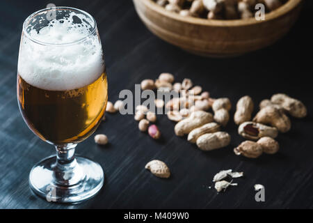 Glas Bier und Erdnüsse auf dem dunklen Hintergrund Stockfoto