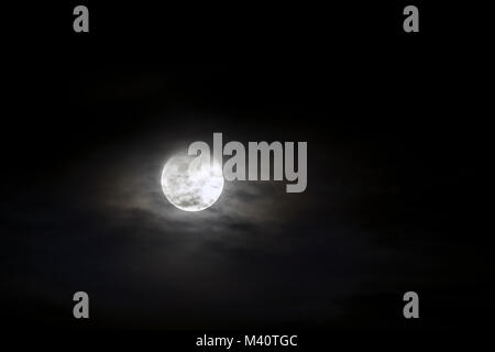 Große silberne leuchtende Mond close-up auf dunklen blauen Himmel mit vereinzelten Wolken. Stockfoto