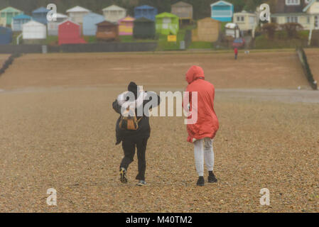 Frauen gehen auf dem Kiesstrand an einem sehr windigen Tag am Tankerton, Whitstable, Kent, Großbritannien. Stockfoto