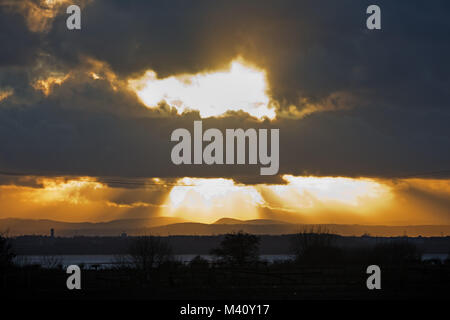 Sonne bricht durch stürmische Wolken bei Sonnenuntergang über den Fluss Mersey Liverpool UK. Stockfoto