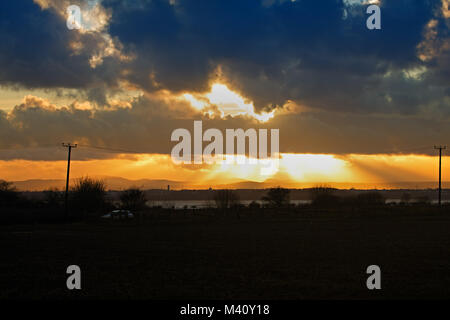 Sonne bricht durch stürmische Wolken bei Sonnenuntergang über den Fluss Mersey Liverpool UK. Stockfoto