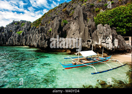 El Nido, Palawan, Philippinen. Philippinisches Boot in Türkis sauberes Wasser mit scharfkantigen Felsen einen Hintergrund. Tropische Land. Weitwinkel Stockfoto