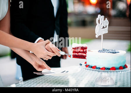 Die Jungvermählten schneiden Sie ein Stück Hochzeitstorte aus rotem Samt. Weißen und Blauen Gradienten Kuchen mit Schild Just Married, Dekoration mit Blaubeeren und Erdbeeren Stockfoto