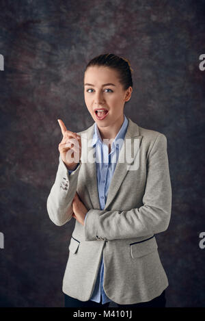 Smart Smiling Young Professional oder Business Frau zeigt mit dem Finger in der Luft mit ein erfreutes Lächeln, als sie eine Lösung für ein Problem findet, oder denkt Stockfoto