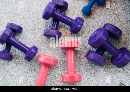 Lila und rosa Hanteln liegen auf dem grauen Fußboden im Fitnessstudio. Stockfoto