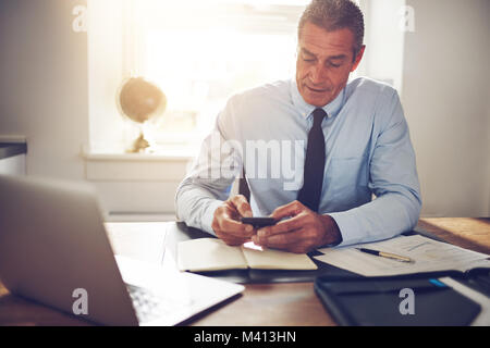 Reifen Geschäftsmann lesen Sms auf seinem Handy, während er an seinem Schreibtisch in einem Büro Stockfoto