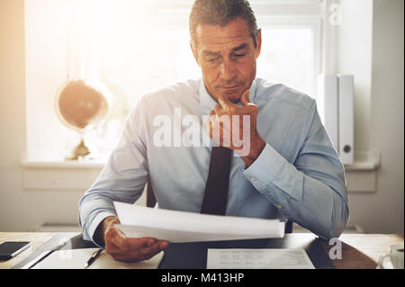 Reifen Rechtsanwalt trägt ein Hemd und Krawatte Lesen von Dokumenten, während allein sitzt an seinem Schreibtisch in einem Büro Stockfoto