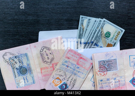 Visa in ausländische Pässe und einen Umschlag mit Geld sind auf einer schwarzen Holztisch. Visa in einen ausländischen Pass. Stockfoto