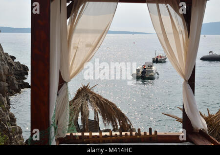 Blick auf ein ruhiges Meer Oberfläche mit Booten von einer Cabana Bett mit weißer Vorhang Stockfoto