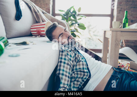 Close up Portrait von Betrunkenen müde bärtigen Hipster mit Mark von Kokain unter die Nase, er schläft auf dem Boden und lehnte sich auf dem Sofa Stockfoto