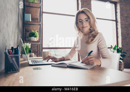 Porträt der Schönen zuversichtlich mit blond gelocktem Haar clevere Frau legere Kleidung, sie sitzt am Tisch vor Computer und prüfen Stockfoto