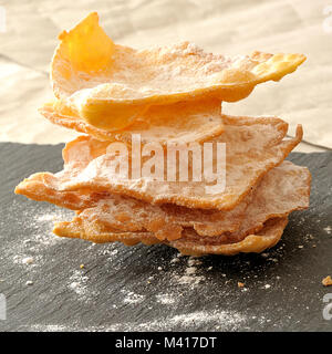 Italienische Dessert für Karneval. Frappe sind süße Krapfen für Karneval vorbereitet. Stapel der Frappe auf einer Schiefertafel Platte, mit Puderzucker, Nahaufnahme, quadratisch Stockfoto