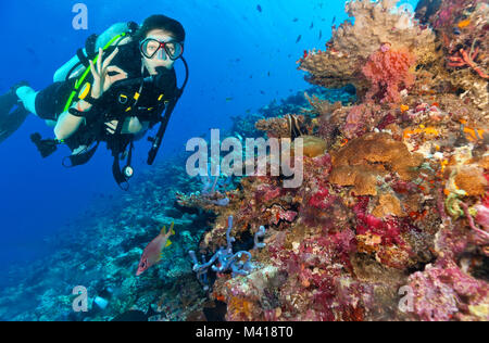 Junge Frau Scuba diver Erkundung Korallenriff und zeigen ok Zeichen, Unterwasser Sport und Aktivitäten Stockfoto