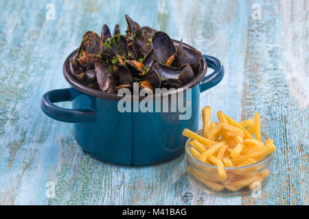 Muscheln in einem blauen Keramik Topf auf einem blauen Hintergrund Holz. Mit einem Glas Schüssel Pommes frites. Brlgium Lebensstil. Stockfoto