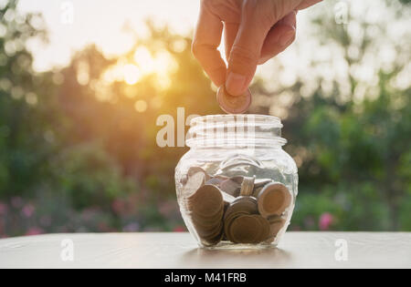 Der Menschen Hand holding Münze und Drop in das Glas. Die Börse in der Buchhaltung Marktwirtschaft Analyse. Stockfoto