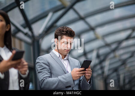 Geschäftsmann anhören Podcast warten auf Zug am Bahnhof Stockfoto