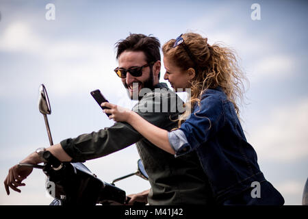 Junges Paar auf dem Motorrad zusammen mit Blick auf Smartphone Stockfoto